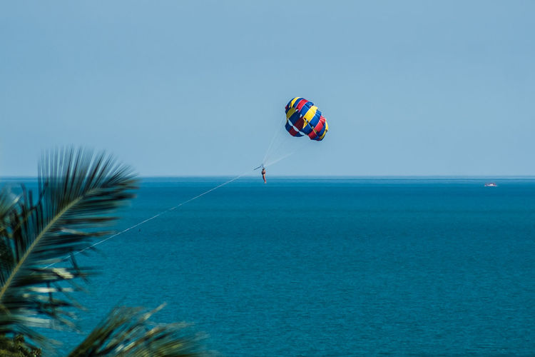 Person parasailing over sea against clear sky