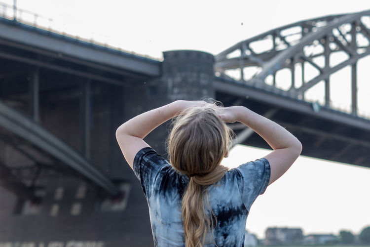 Rear view of girl standing by bridge against clear sky