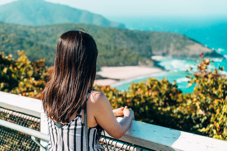 Rear view of woman looking at sea while standing by railing during sunny day
