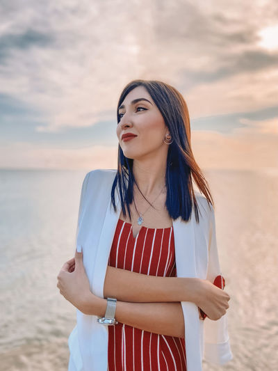 Beautiful young woman standing by sea against sky