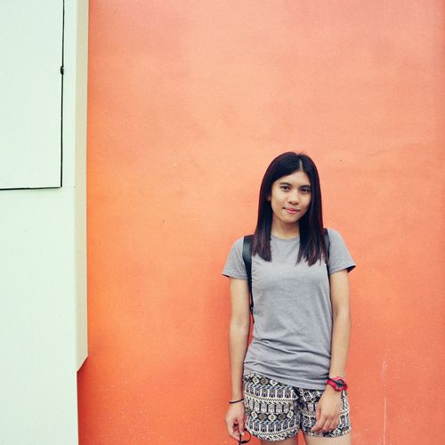 Portrait of smiling young woman standing against orange wall
