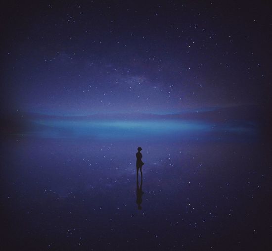 Man standing in sea against sky at night