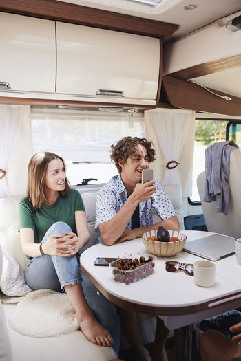 Smiling siblings relaxing at table in motor home during summer vacation