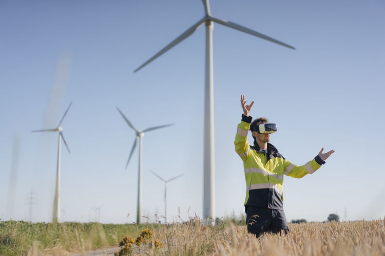 Engineer standing in a field at a wind farm wearing vr glasses