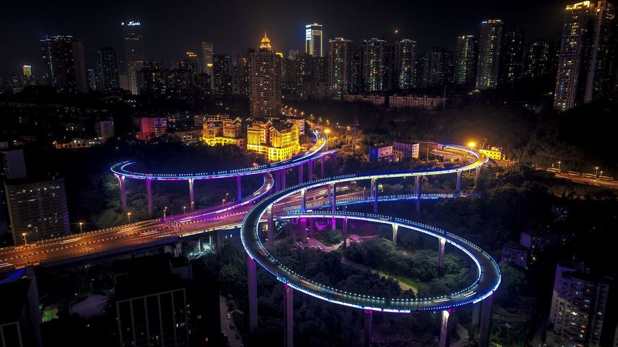 Aerial view of illuminated elevated road by buildings at night