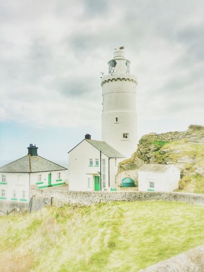 Lighthouse on field against cloudy sky