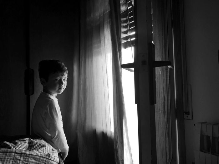 Portrait of boy standing by window at home