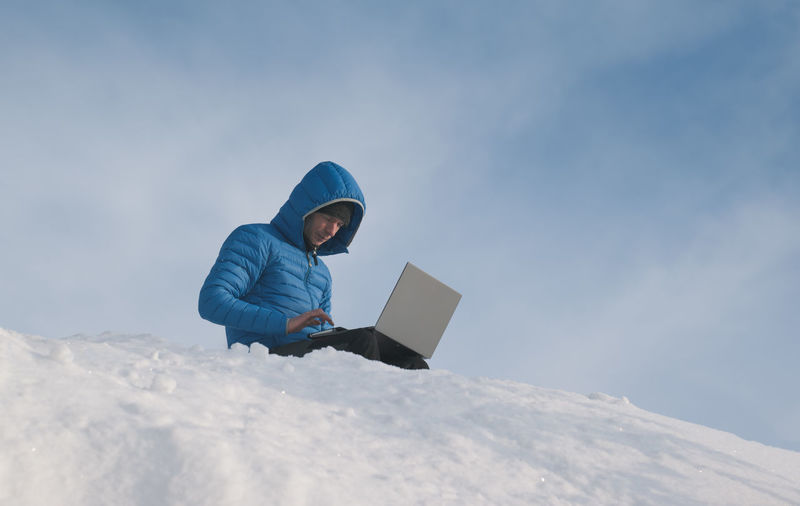 Rear view of man using digital tablet while sitting on snow