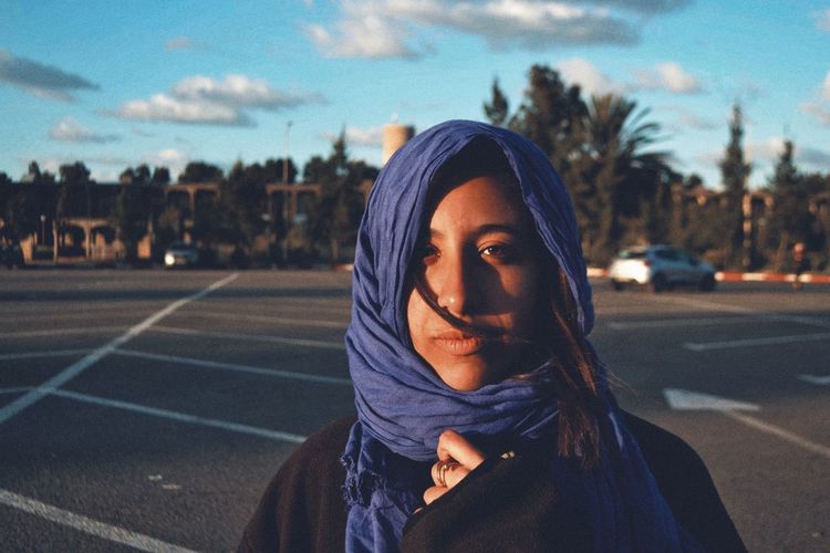 Close-up portrait of teenage girl standing on road against sky