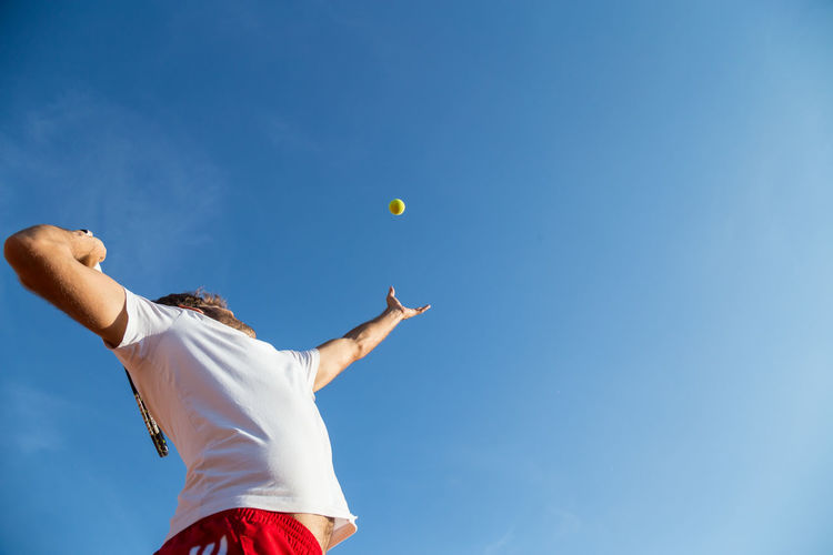 Low angle view of man playing with ball against blue sky