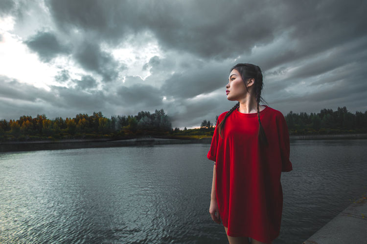 Woman looking away while standing by lake against sky