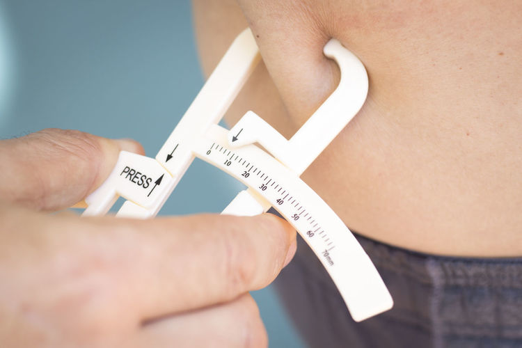 Midsection of person checking belly fat with caliper