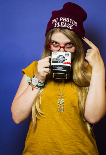 Young woman wearing knit hat while drinking coffee against blue background
