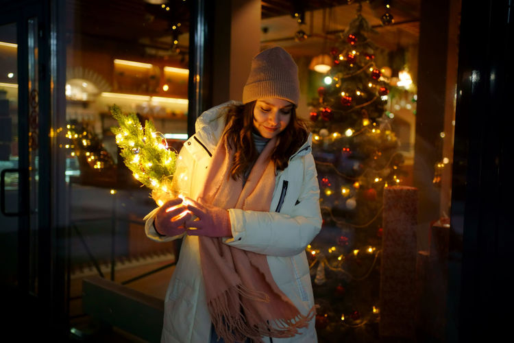 Portrait of young woman standing against illuminated christmas tree