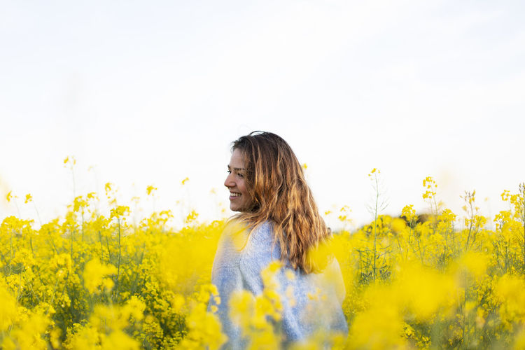 Young woman with yellow flowers in field against sky