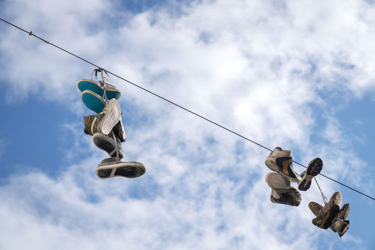 Low angle view of shoes hanging on rope against cloudy sky