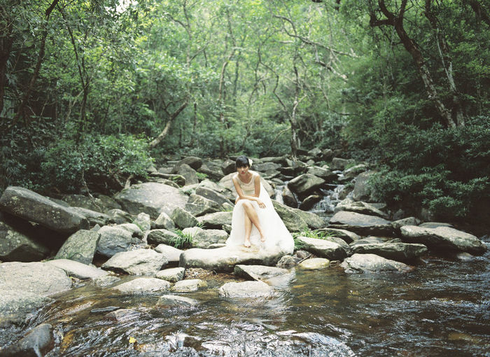 Woman sitting on rock by stream in forest