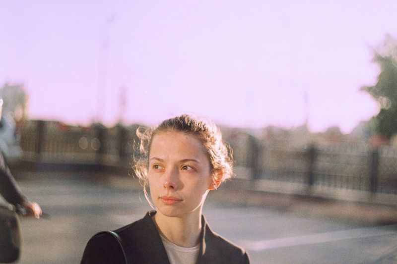 Portrait of young woman looking away in city against sky