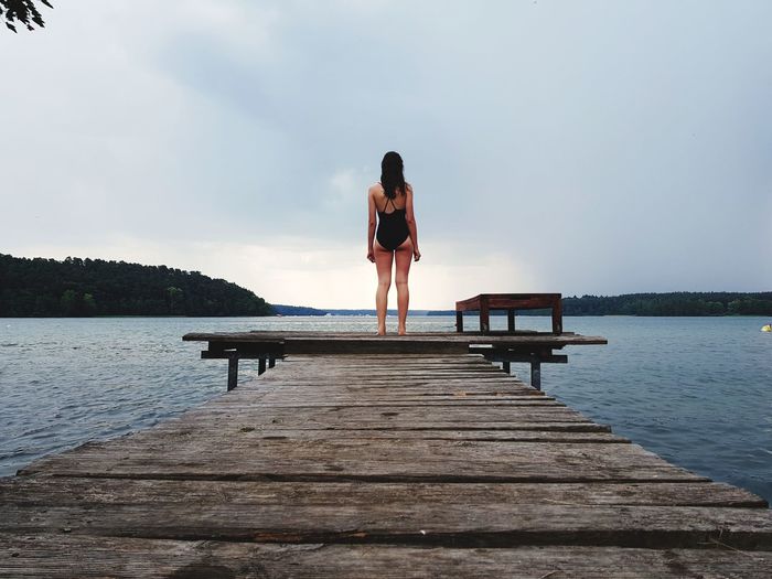 Rear view of teenage girl standing on pier over lake against sky