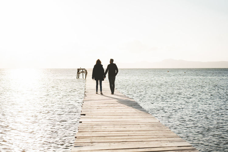 Couple holding hands walking on jetty over sea