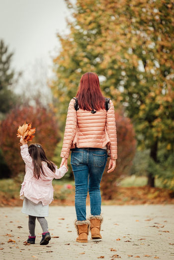 Rear view of mother and daughter walking on road