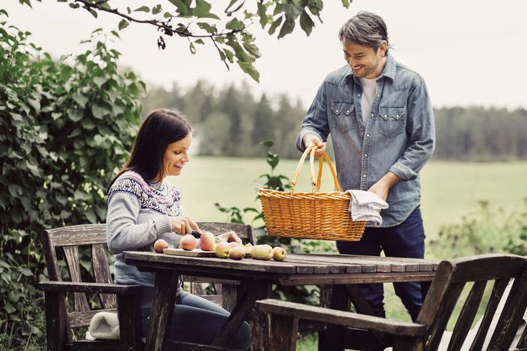 Happy man placing basket on table while woman cutting apples at organic farm