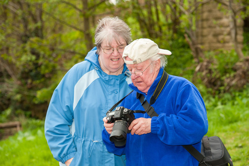 Man photographing woman holding camera while standing outdoors