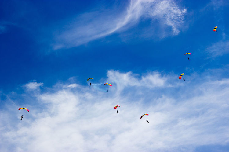Low angle view of people paragliding against sky