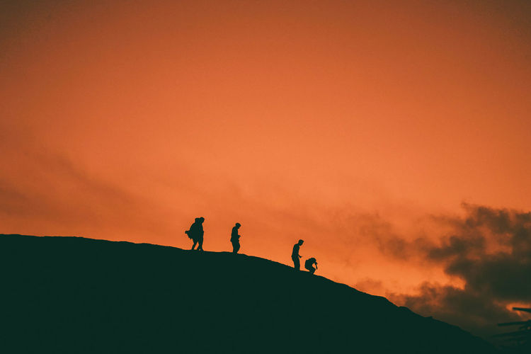 Silhouette people on mountain against orange sky