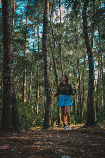 Full length of woman standing amidst trees in forest