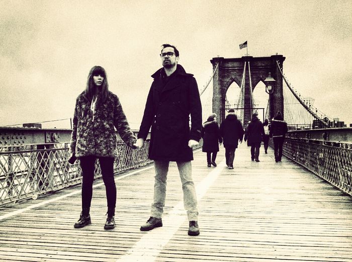 Couple holding hands on footbridge against sky