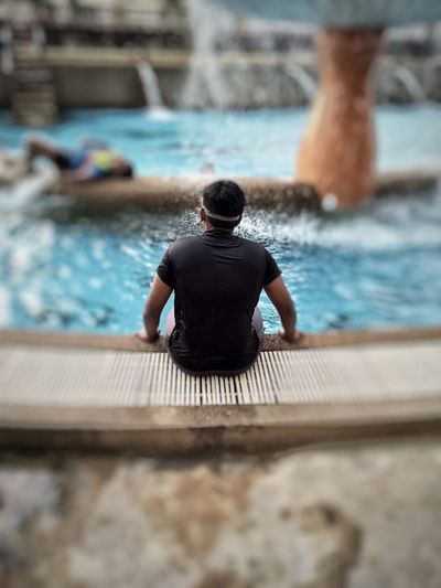 Rear view of man sitting in swimming pool