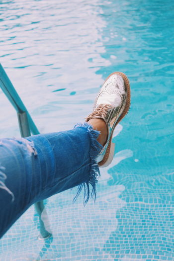 Low section of woman wearing shoe over swimming pool
