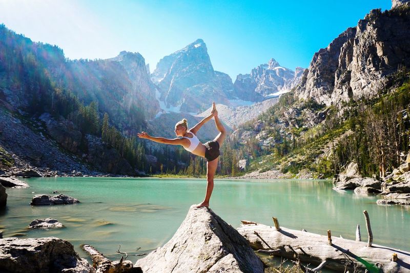 Woman doing yoga on rock by lake against mountains