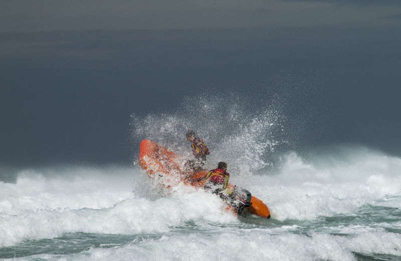 People in lifeboat on sea with splashing wave