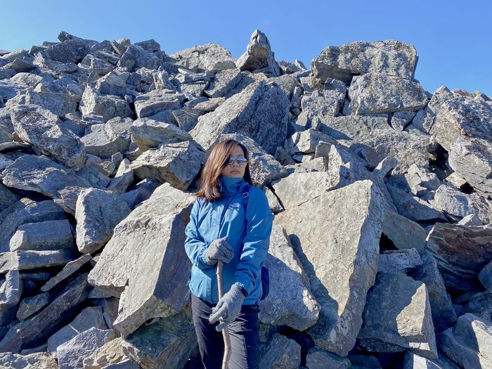 Woman standing on rock against blue sky