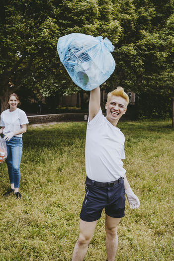 Cheerful male volunteer showing plastic bag while cleaning in park