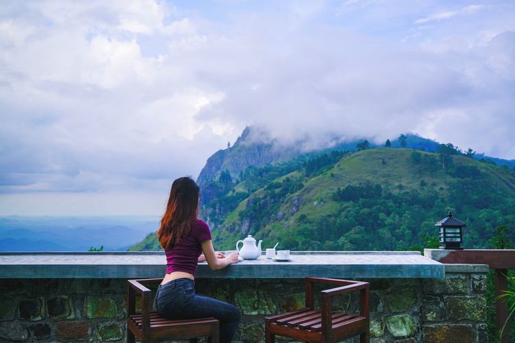 Woman sitting at table against sea and mountains
