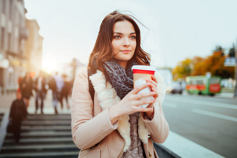 Thoughtful young woman holding disposable coffee cup on street