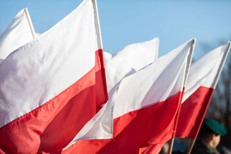 Polish flags are flying and in the background stands a soldier in uniform and a green beret.