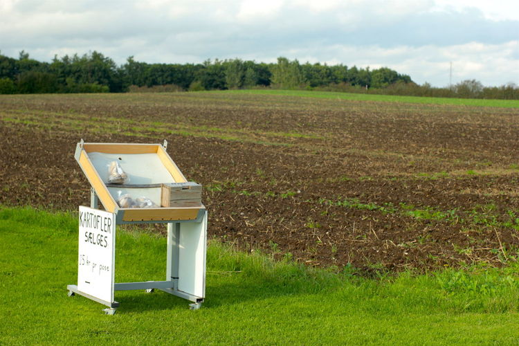 Potatoes for sale on stall at field against cloudy sky