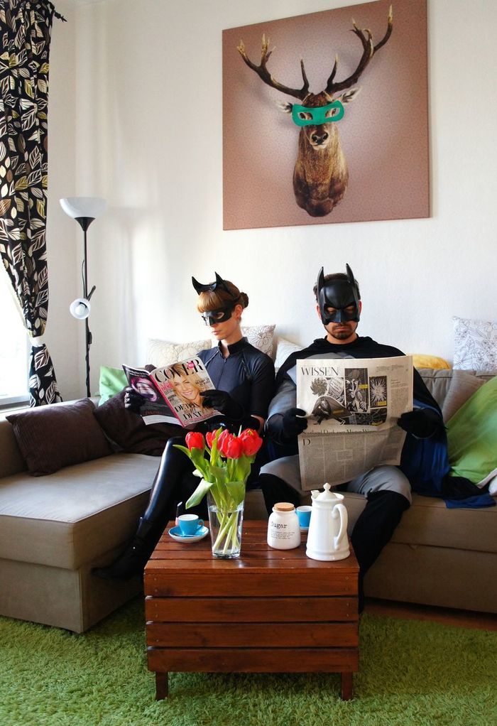 Couple in batman costumes reading newspapers at home