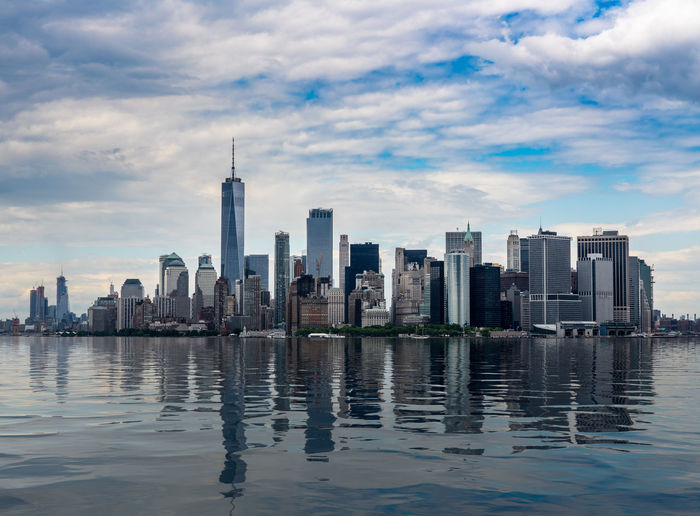 River and modern buildings in city against cloudy sky