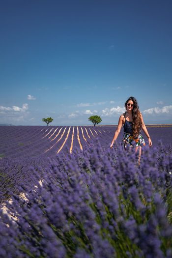 Woman standing on field by purple flowering plants against sky