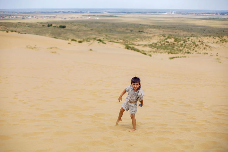 Boy is child traveler in a suit of an archaeologist tracker and wearing hat walk sand in the desert