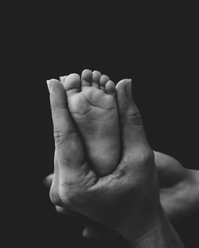 Close-up of human hand and baby foot against black background