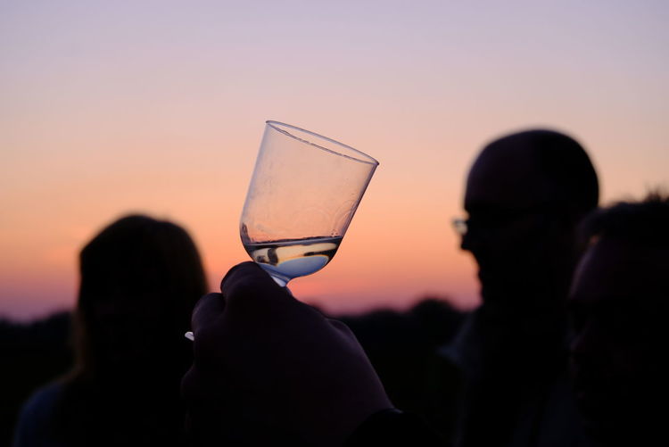 Close-up of silhouette man drinking glass against sunset sky
