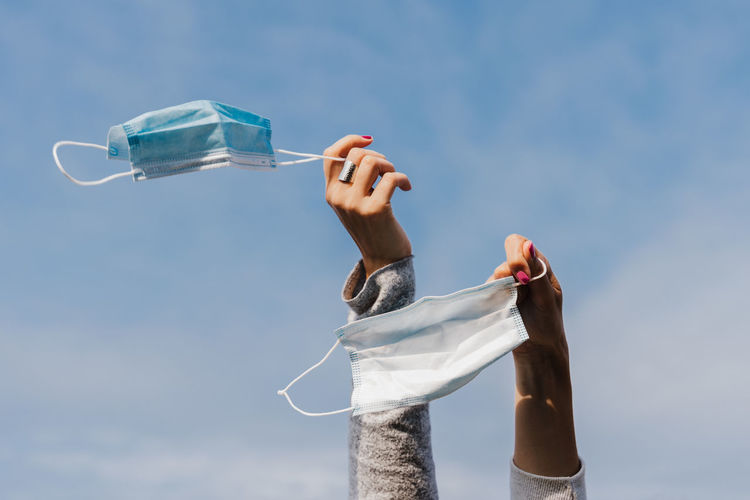 Low angle view of man holding bottle against blue sky