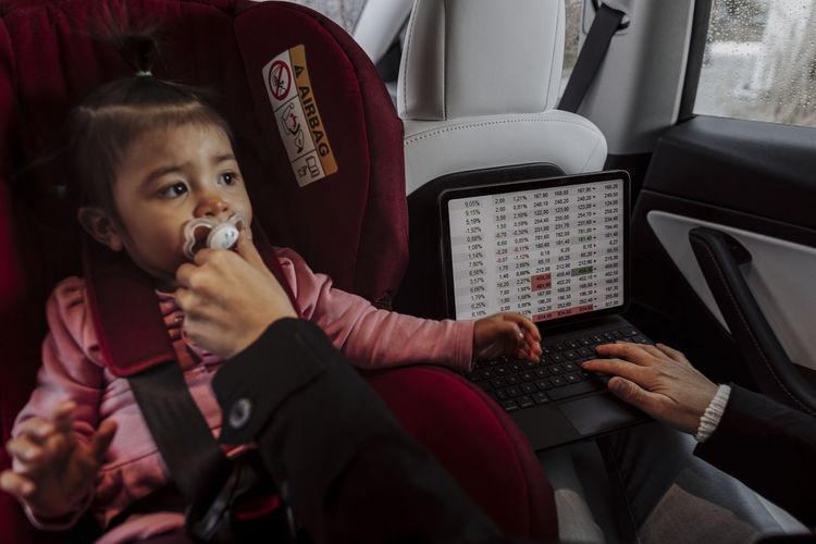 Baby girl sitting in car seat while mother using laptop