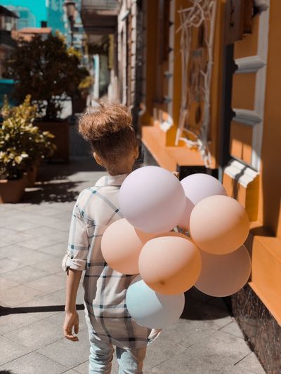 Rear view of boy with balloons walking in city